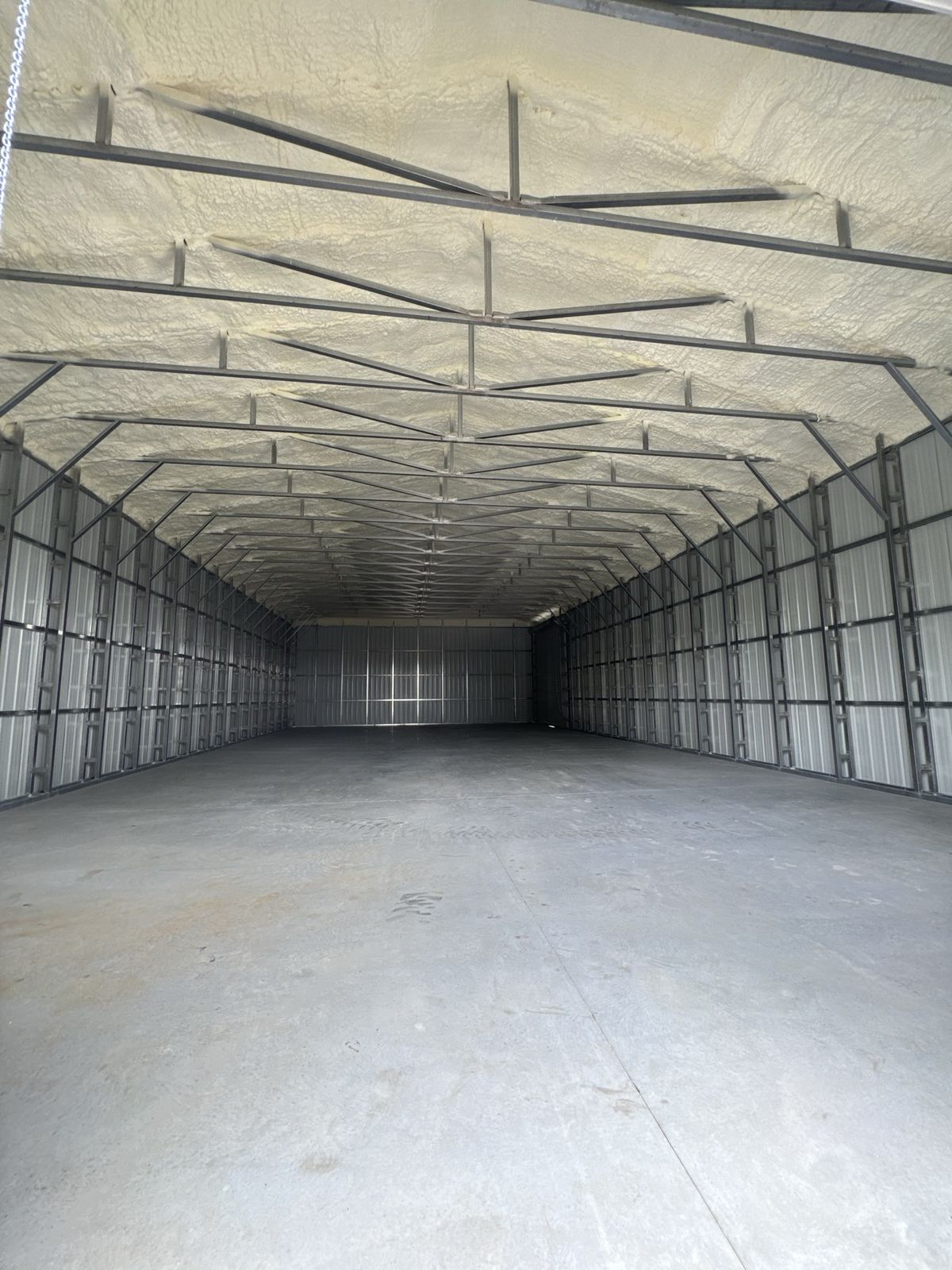 Spray foam applied to the roof and upper sidewalls of a steel metal building, with bare steel framing still visible below