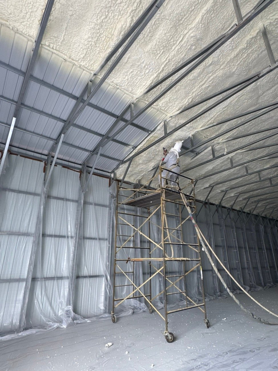 Ideal Insulation crew member on scaffolding spraying foam insulation on the roof of a metal building