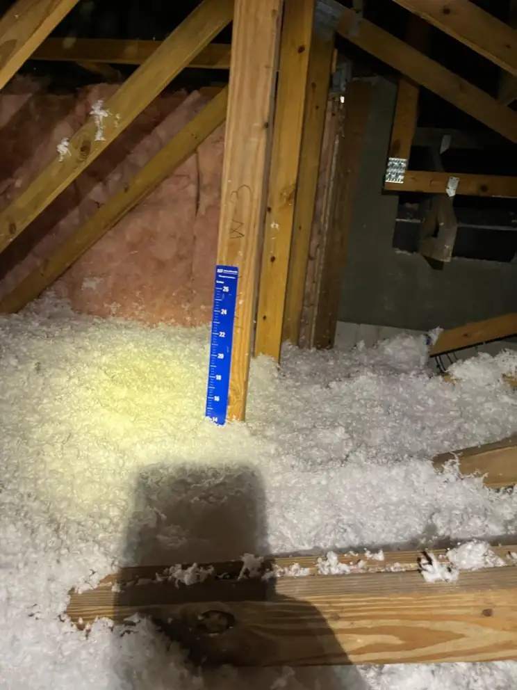 Blown-in fiberglass in a Naples attic with a blue depth ruler staked in the insulation